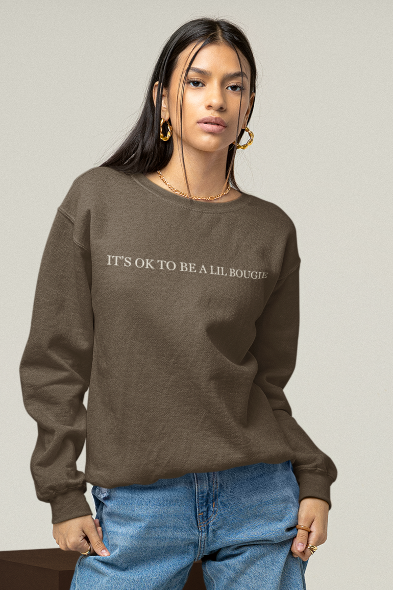 Model wearing brown Bougie crewneck with “It’s OK to Be a Lil Bougie” printed across front.