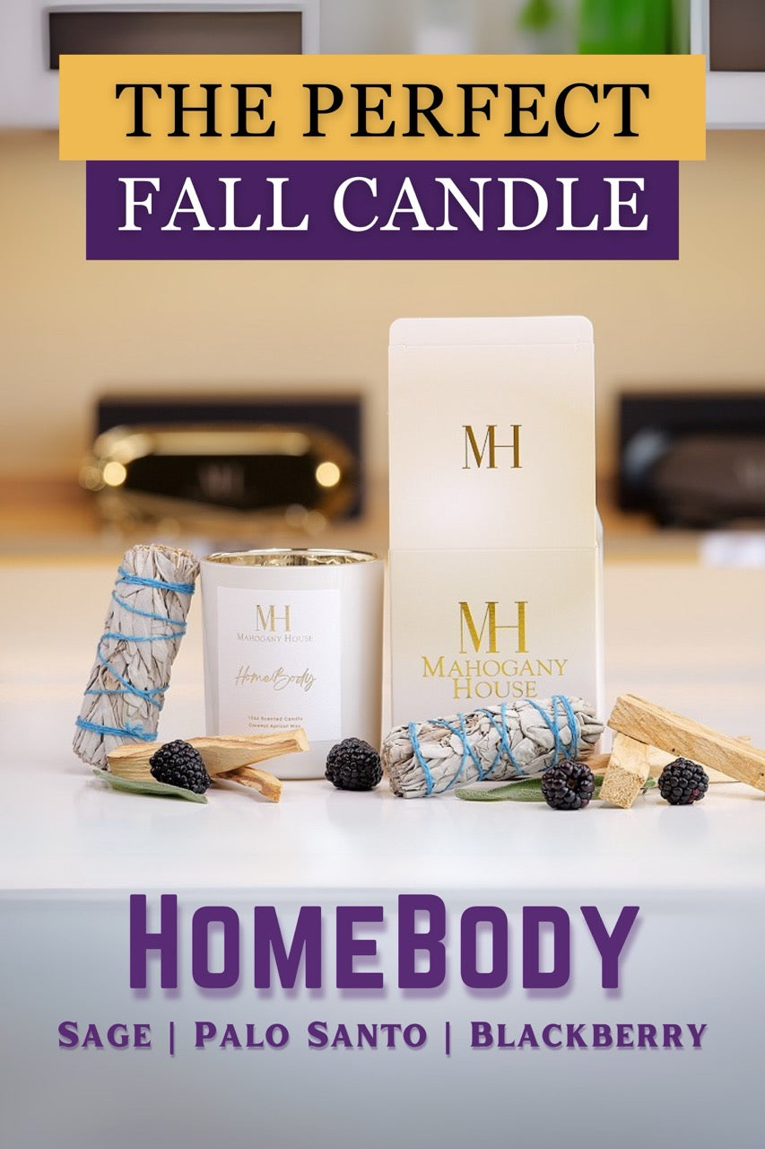 HomeBody votive candle in white glass vessel with Mahogany House packaging, styled with palo santo, sage bundles, and blackberries on a purple background.