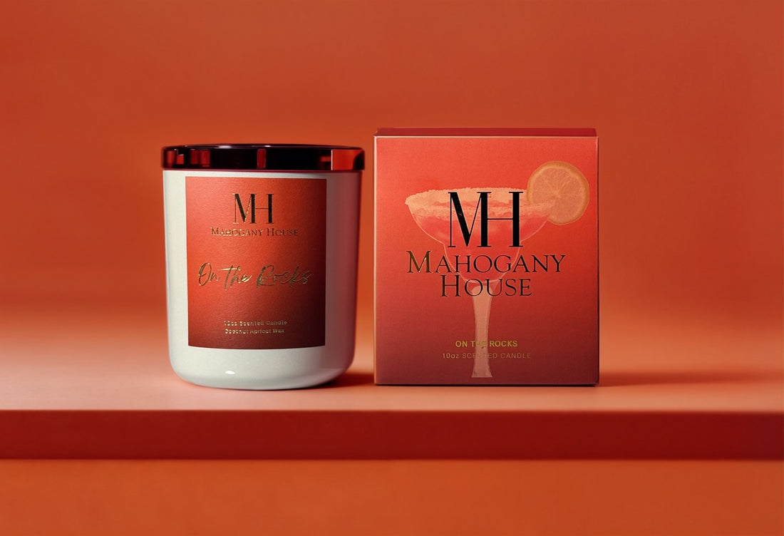 On The Rocks 10oz wooden wick candle in cream glass vessel with red label, displayed beside Mahogany House packaging on a red background.