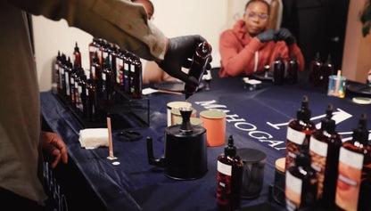 Person pouring fragrance oil from a premium bottle into a jigger as a demonstration for the attendees of a candle making class