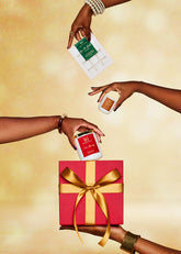 Three hands reaching towards three different scented candles with a red gift box featuring a gold ribbon on a yellow background.