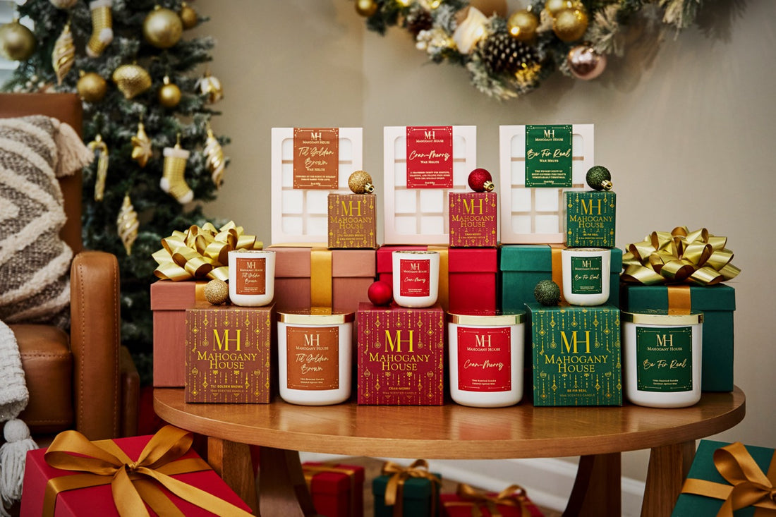 Collection of Christmas-themed candles and gift boxes on a table with a decorated tree in the background.