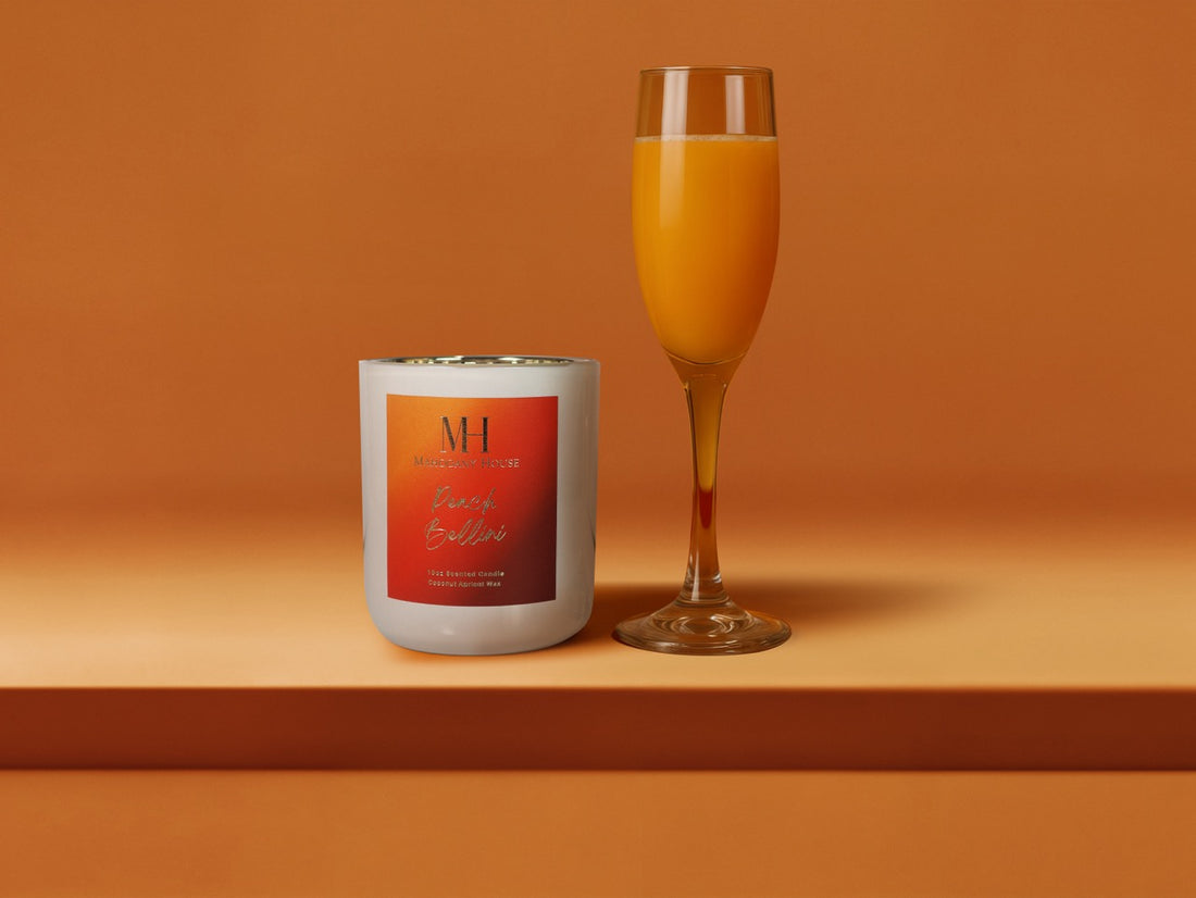 Peach Bellini 10oz wooden wick candle in white glass vessel with orange label, styled beside a champagne flute of sparkling prosecco on an orange background.