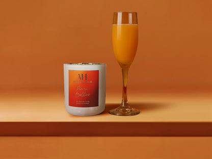 Peach Bellini 10oz wooden wick candle in white glass vessel with orange label, styled beside a champagne flute of sparkling prosecco on an orange background.