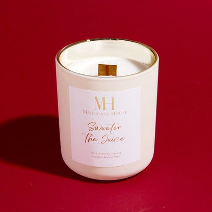 Unlit Sweeter The Juice 10oz wooden wick candle in white glass jar with gold lid, displayed on a red background.