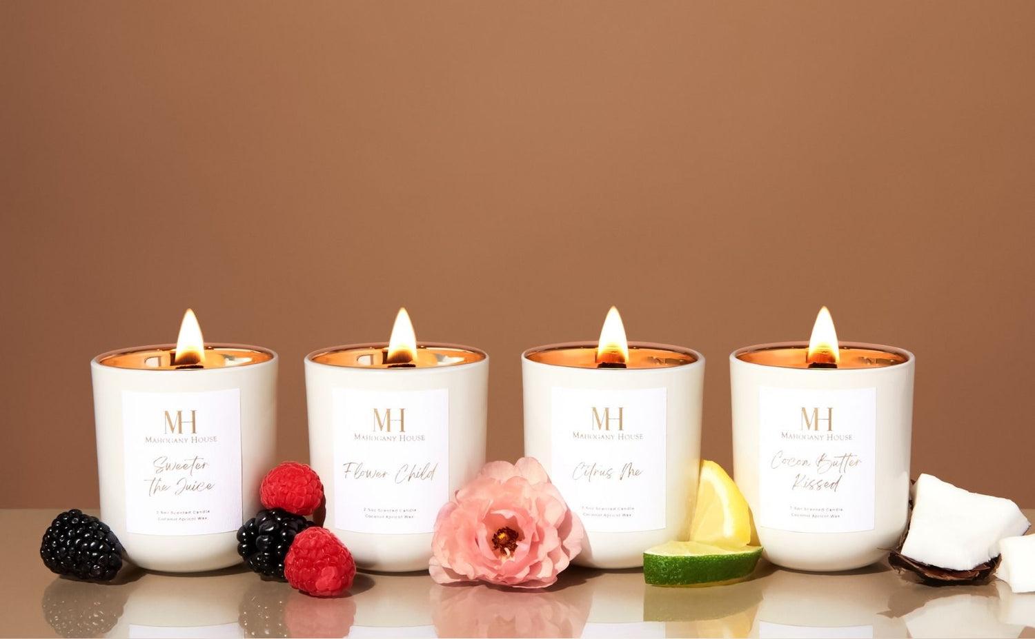 Four lit candles with visible brand logo on a reflective surface against a brown background